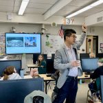 adult raises their hand while students watch