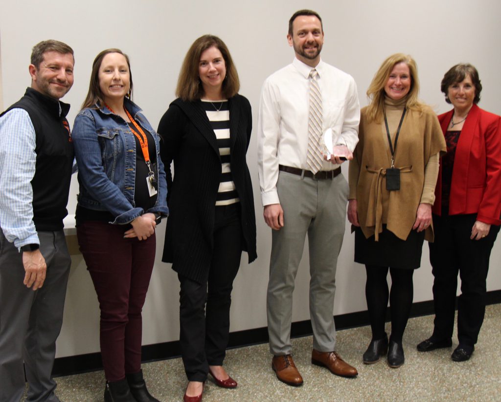 six people pose for photo with teacher holding award