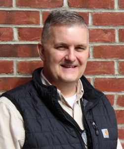 person in black vest in front of brick wall