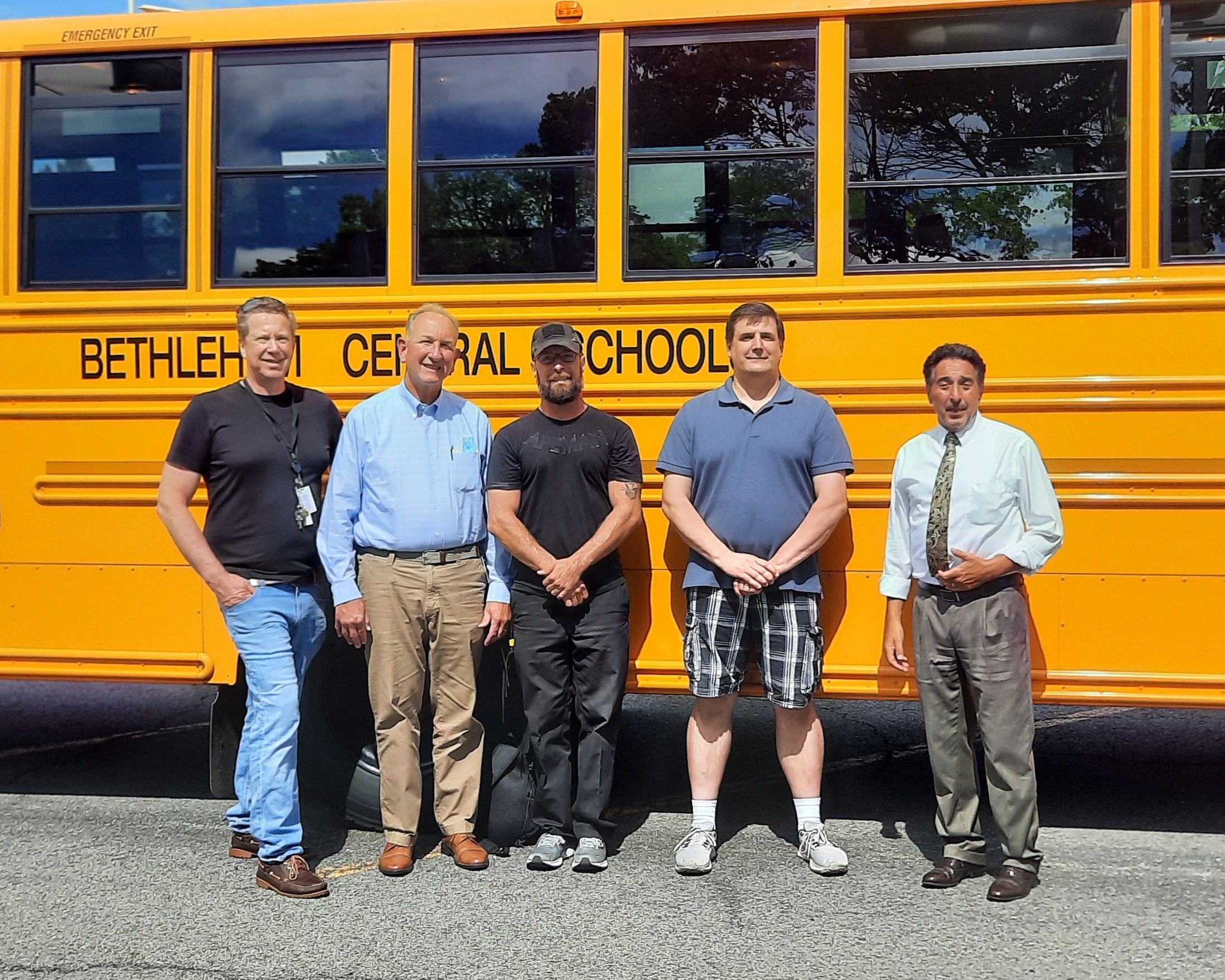 five people pose in front of school bus
