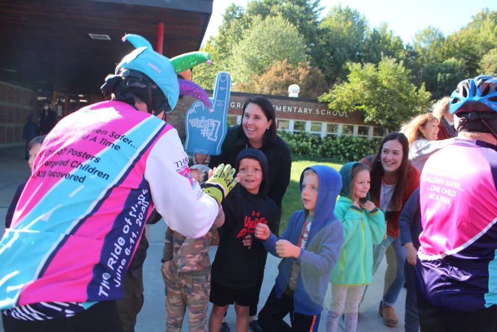 students cheer on bike rider, hold foam finger