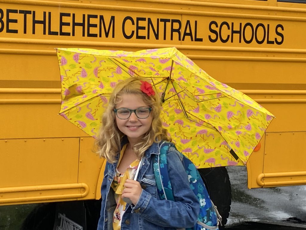 student with yellow umbrella in front of yellow bus