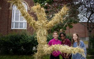 Three students pose with scarecrow they built outside of the middle school.