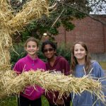 Three students pose with scarecrow they built outside of the middle school.