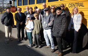 Family of David Burtis poses with BC bus drivers and staff in front of electric school bus.