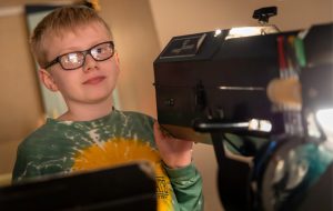 A student stands behind a spotlight as they work as a member of the crew for an upcoming theater production