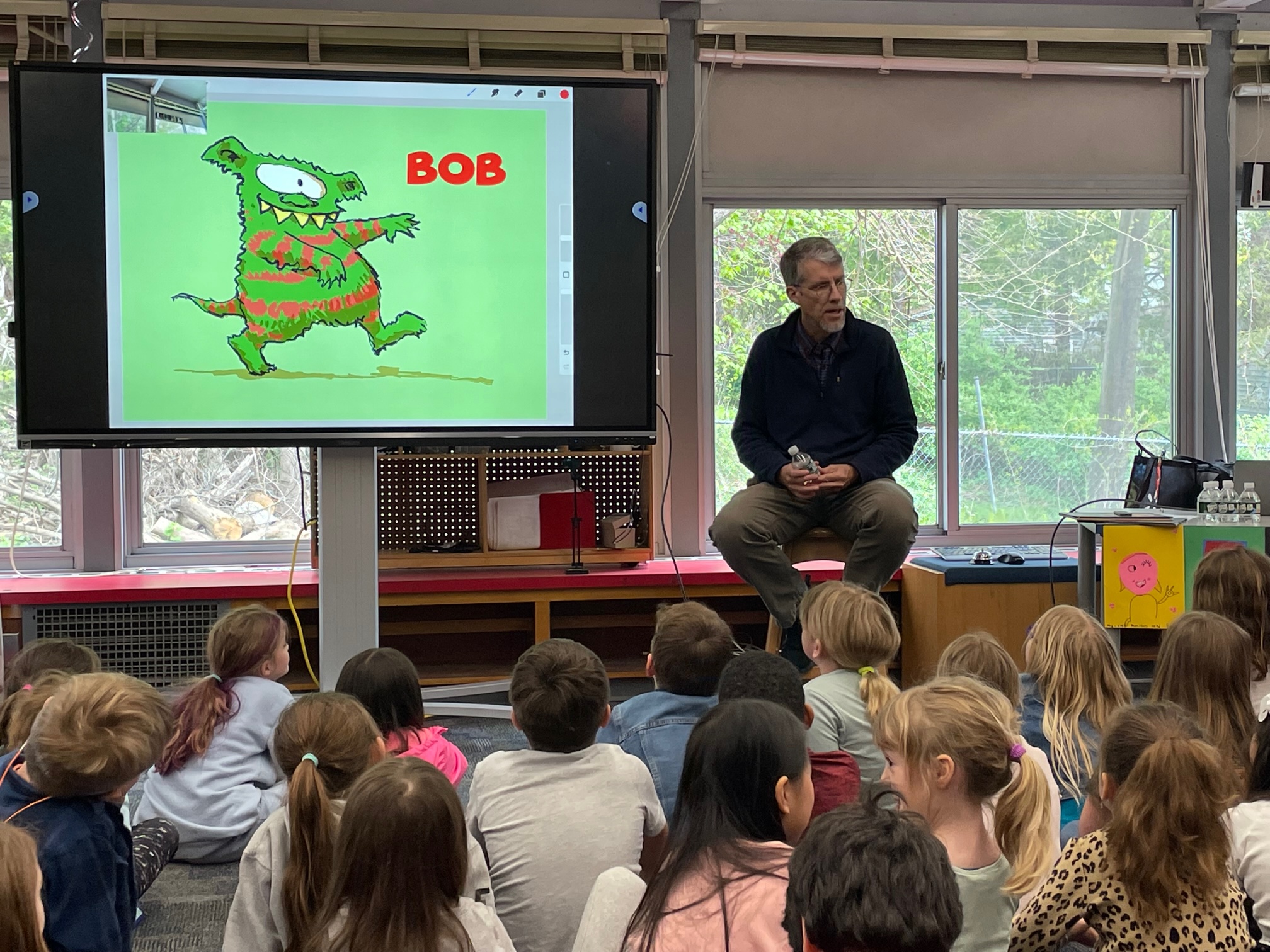 Photo of Matt McElligott with the illustration of Bob as students look on