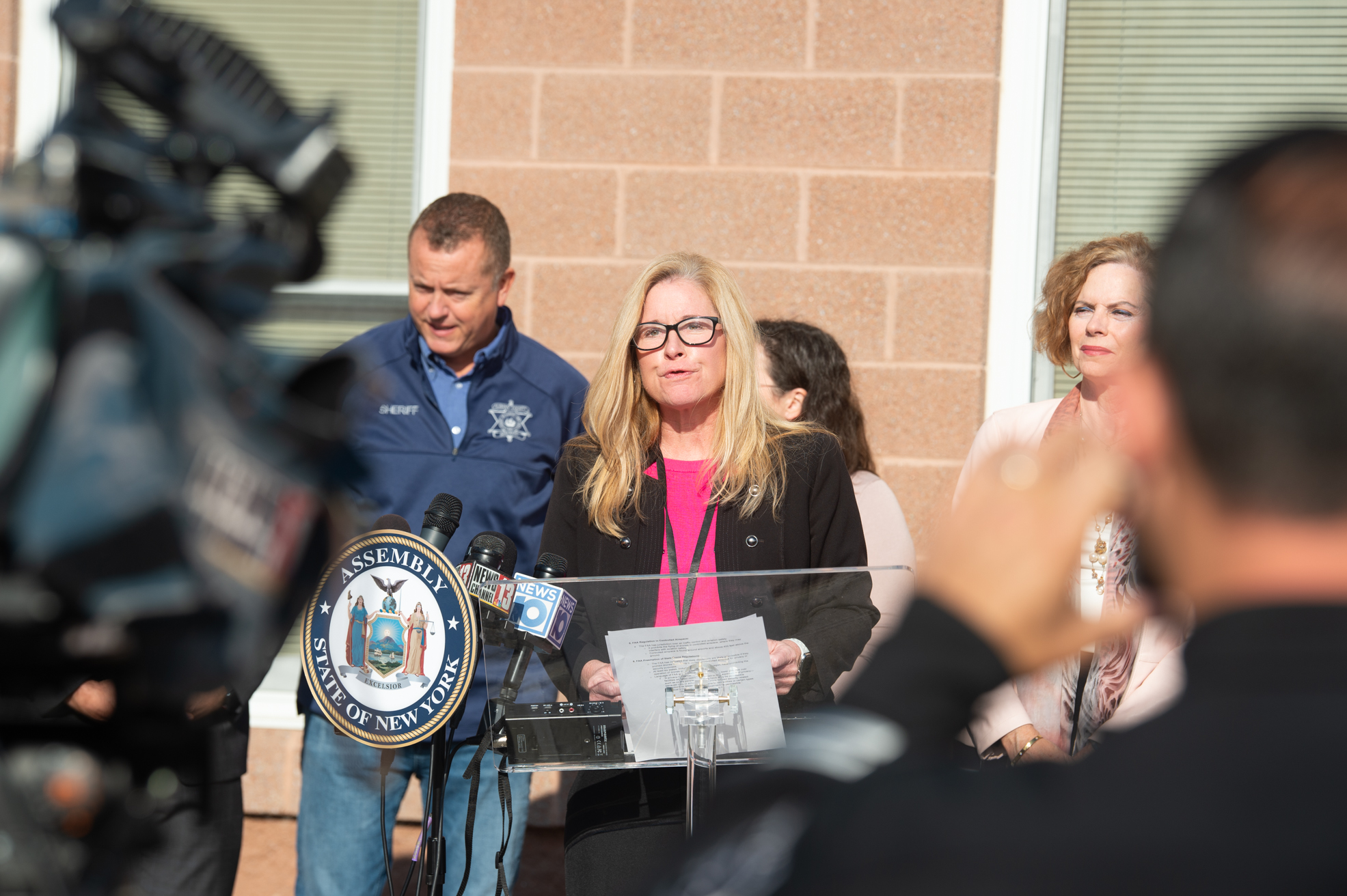 woman speaks at microphone with cameras