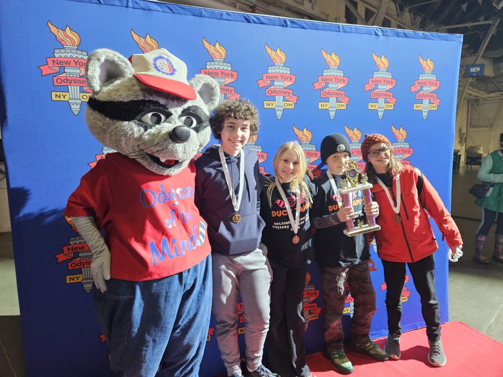 students wearing medals and smiling next to a mascot