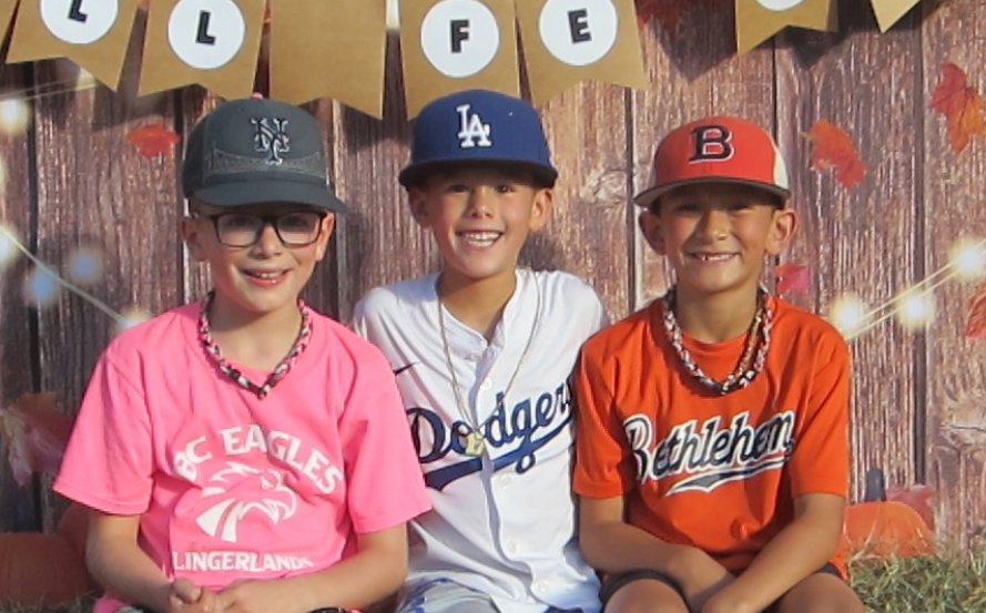 three students in baseball hate and jerseys in front of fall decorations